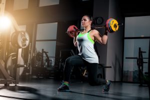 Fit young woman lifting barbells looking focused, working out at a gym