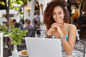 photo-glad-adorable-curly-african-woman-sits-front-opened-laptop-computer-sidewalk-cafe-satisfied-make-good-presentation_273609-3488